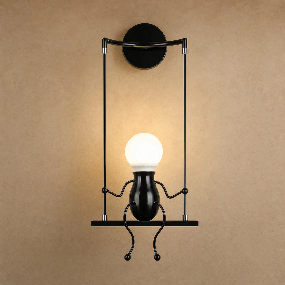 Applique murale noire Girotta, petit personnage assis sur sa balançoire, ampoule globe allumée