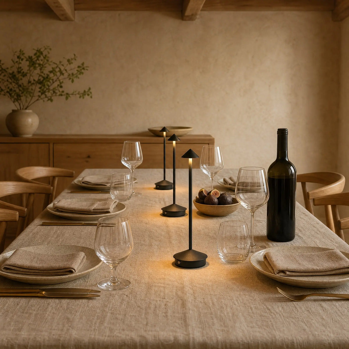 Trois lampes de table sans fil noires alignees sur une table dressee le soir