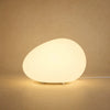 Lampe à poser galet lumineux Sassolia allumée en blanc chaud sur fond minéral sable