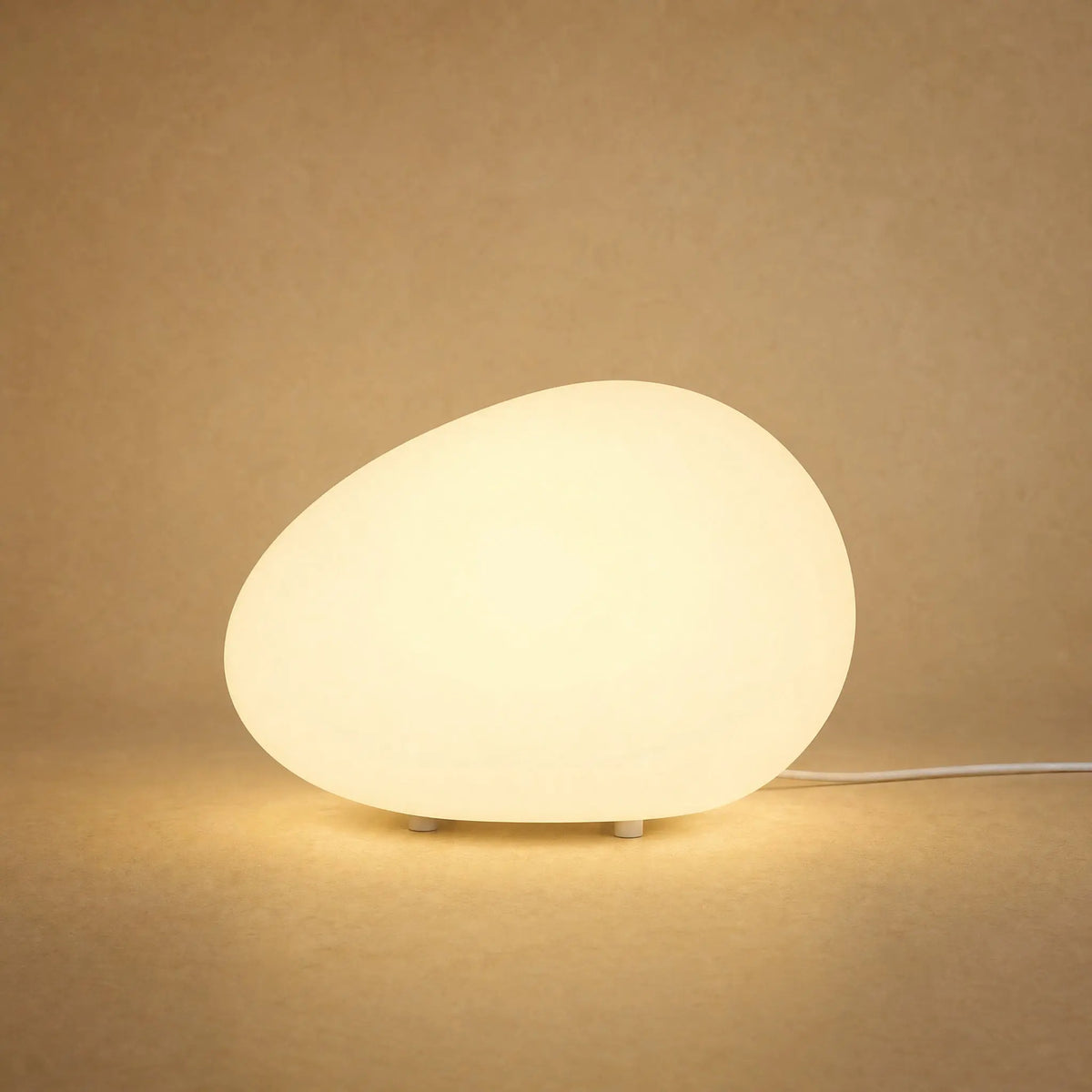 Lampe à poser galet lumineux Sassolia allumée en blanc chaud sur fond minéral sable