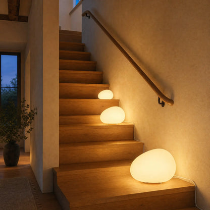 Trois lampes galet Sassolia de trois tailles allumées sur les marches d'un escalier en chêne