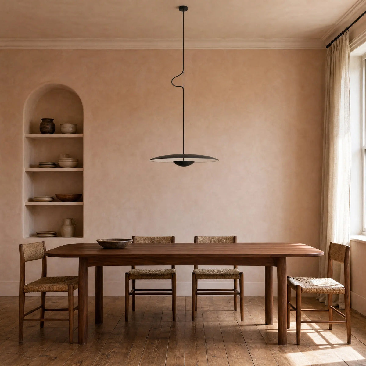 Suspension noire au-dessus d'une table de noyer dans une salle à manger aux murs ocre