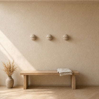 Trois appliques murales en pierre alignées au-dessus d'un banc de chêne dans une entrée, lumière naturelle | Delvanie